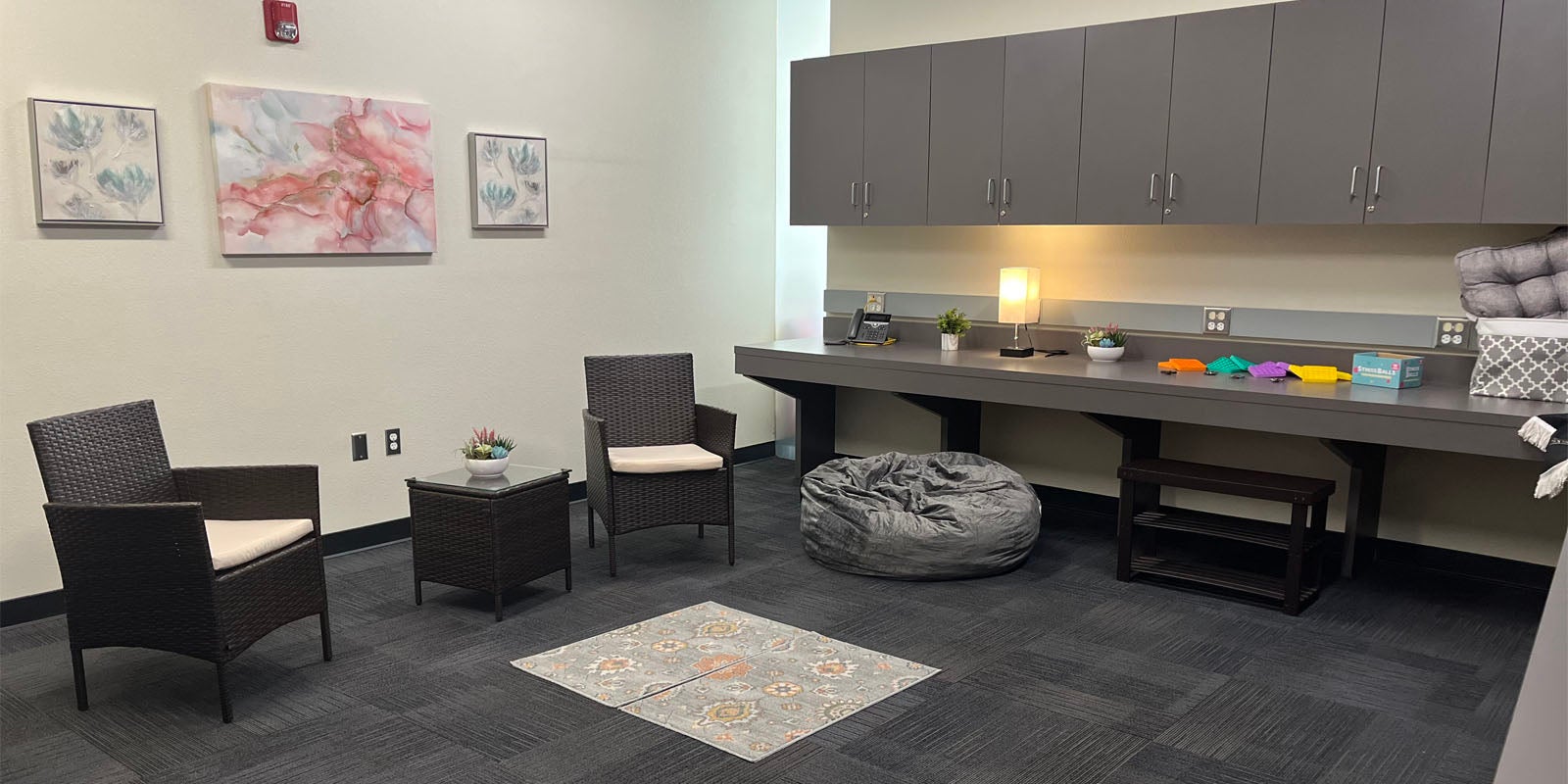 Reflection room with two chairs, a table, three pictures on the wall, two rugs, pillows, a bean bag chair, and electric candle