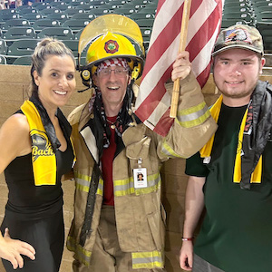 Three people posing with the American flag. The middle person is a firefighter.