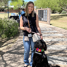 A blonde woman with her service dog standing in the middle of a sidewalk