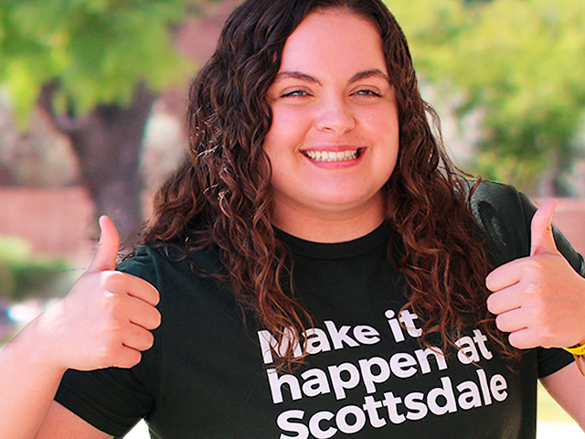 SCC student holding two thumbs up and wearing a Make it happen at Scottsdale tshirt