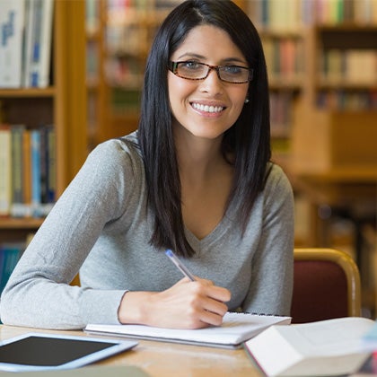 student using computer, pen, paper, books to do research in a library