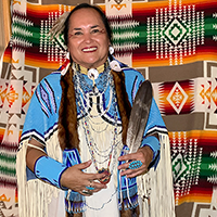 imy, She Laughs a Lot, is an Indigenous elder. Tia is wearing Northern traditional buckskin regalia in shades of blue and cream.