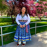 Diedre’ is wearing a traditional three-tiered masani skirt with floral designs and blue, yellow, white ribbon. She is also wearing buckskin wrap moccasins, traditional Navajo sash belt, silver concho belt and Navajo squash blossom jewelry in turquoise. 