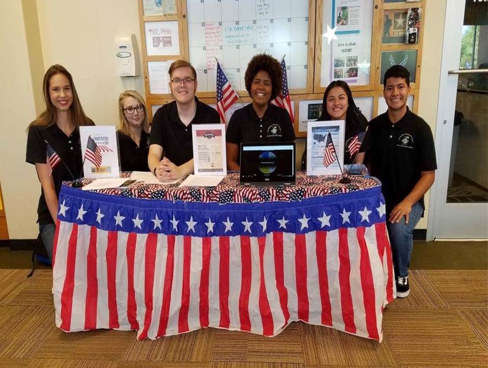 civic-minded students posing behind a table with patriotic regalia on it