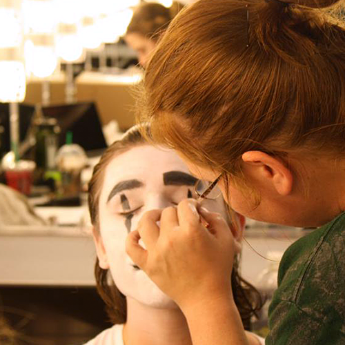 student applying white makeup to the face of a student