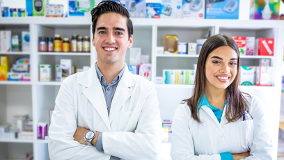 male and female pharmacy technicians in a pharmacy with pills on shelves behind them