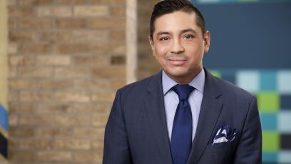 Man with blue suit and blue tie smiling into the camera