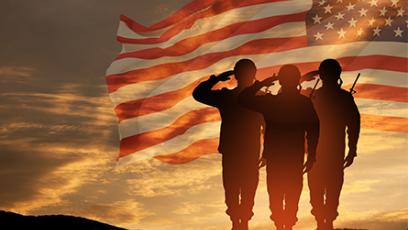 military personnel standing on a hill saluting with a flag superimposed over the sunset