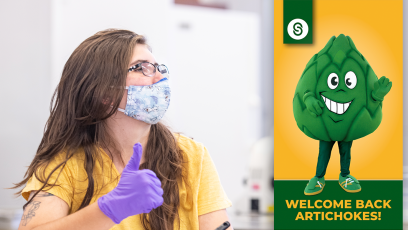 student wearing face mask and gloves with thumb up looking at Welcome Back Artichokes graphic