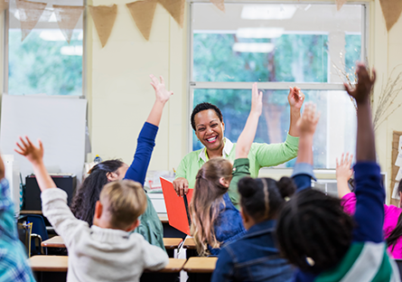 teacher facing classroom of students with raised hands 