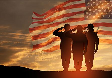 military personnel standing on a hill saluting with a flag waving over the sunset background