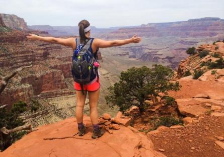 A photo of a backpacking woman T-posing at the edge of a vast desert canyon, green trees are in the valley below.