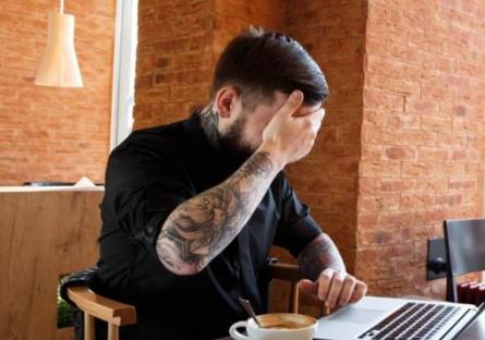 man covering eyes while looking at laptop