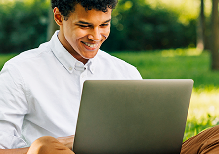 smiling student with laptop sitting on the grass on a beautiful campus