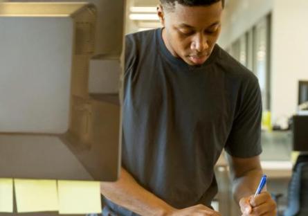 Young man making notes by a computer