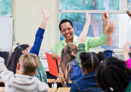 teacher facing classroom of students with raised hands 