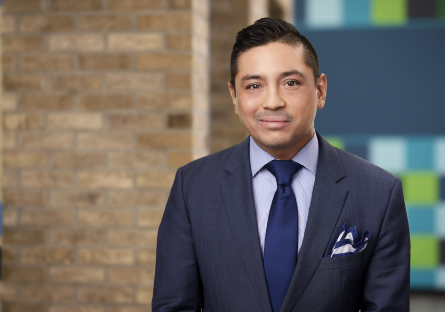 Man with blue suit and blue tie smiling into the camera