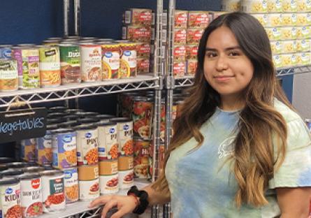 student standing in front of stocked shelves in the food pantry