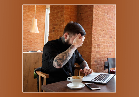 man covering eyes while looking at laptop