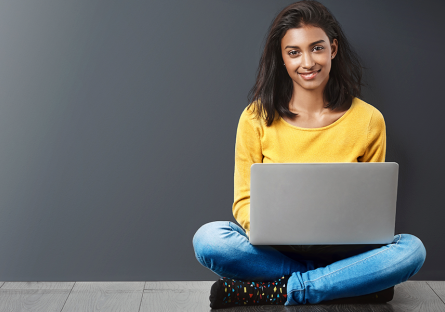 student sitting on wood floor holding laptop