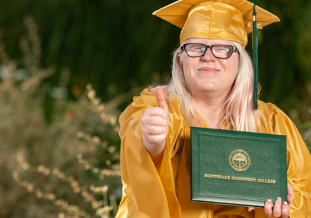 older adult graduate holding diploma and indicating happiness with a thumbs up