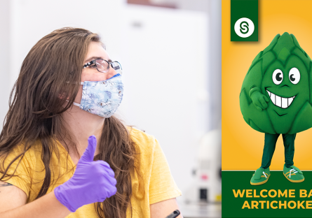 student wearing face mask and gloves with thumb up looking at Welcome Back Artichokes graphic