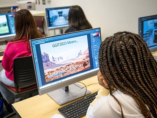 student looking at computer screen that displays the words, GGIT2023 Means, over a desert background