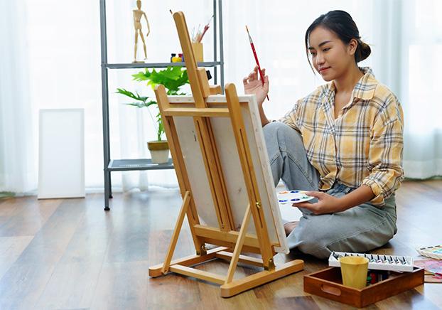 student sitting on the floor painting on an easel
