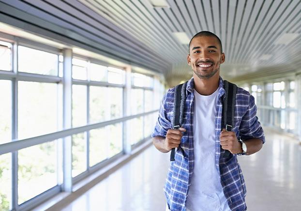 student with backpack walking down brightly lit hallway toward class