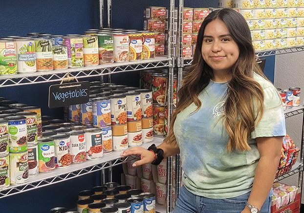 student standing beside pantry shelves stocked with canned goods