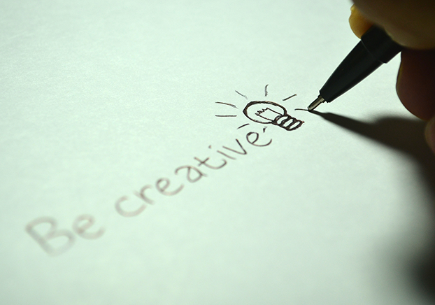 The words, Be creative, handwritten on paper with a light bulb.