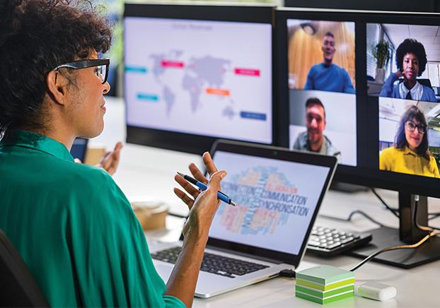 Instructor looking a computer screen. There are two displays and one and a laptop screen. One of the screens shows a virtual meeting with four participants.