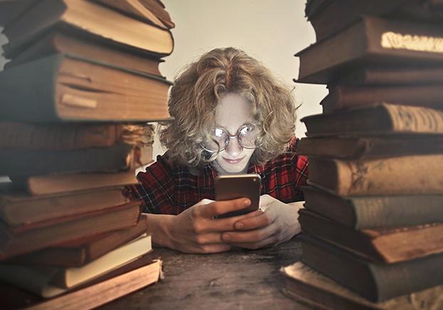 student reading a book at a table surrounded by piles books