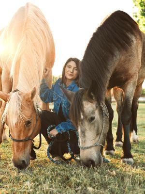 Erin Perre sitting on the grass with 2 horses beside